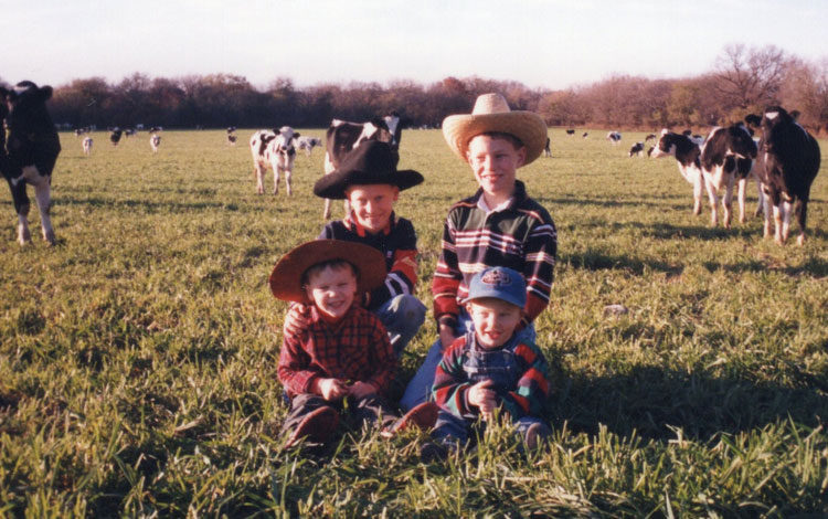 Four young boys pose in a dairy cattle pasture.